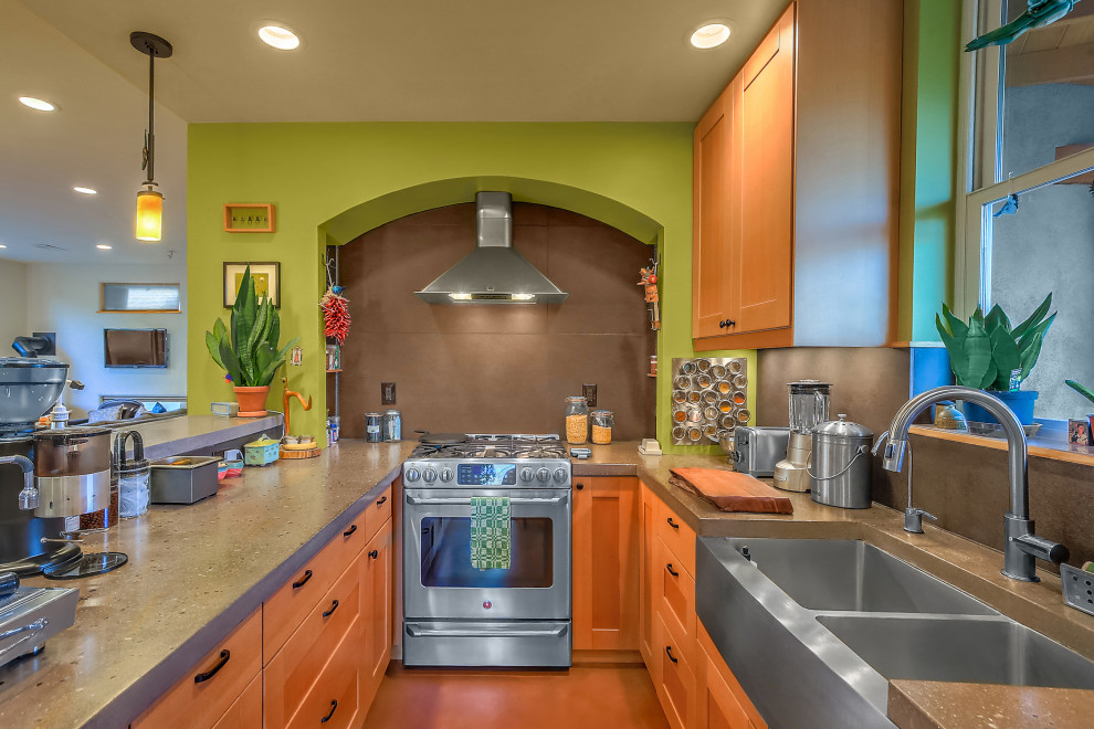 Photo of a small tropical u-shaped eat-in kitchen in Albuquerque with a farmhouse sink, recessed-panel cabinets, medium wood cabinets, concrete benchtops, grey splashback, stainless steel appliances, concrete floors, with island, multi-coloured floor and grey benchtop.