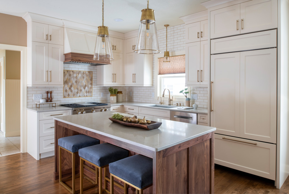 This is an example of a mid-sized transitional l-shaped eat-in kitchen in Minneapolis with an undermount sink, shaker cabinets, quartz benchtops, with island, white cabinets, white splashback, subway tile splashback, stainless steel appliances, medium hardwood floors, brown floor and white benchtop.