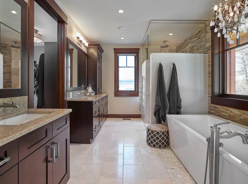 This is an example of a large transitional master bathroom in Edmonton with shaker cabinets, dark wood cabinets, a freestanding tub, an alcove shower, a two-piece toilet, beige tile, porcelain tile, beige walls, travertine floors and an undermount sink.