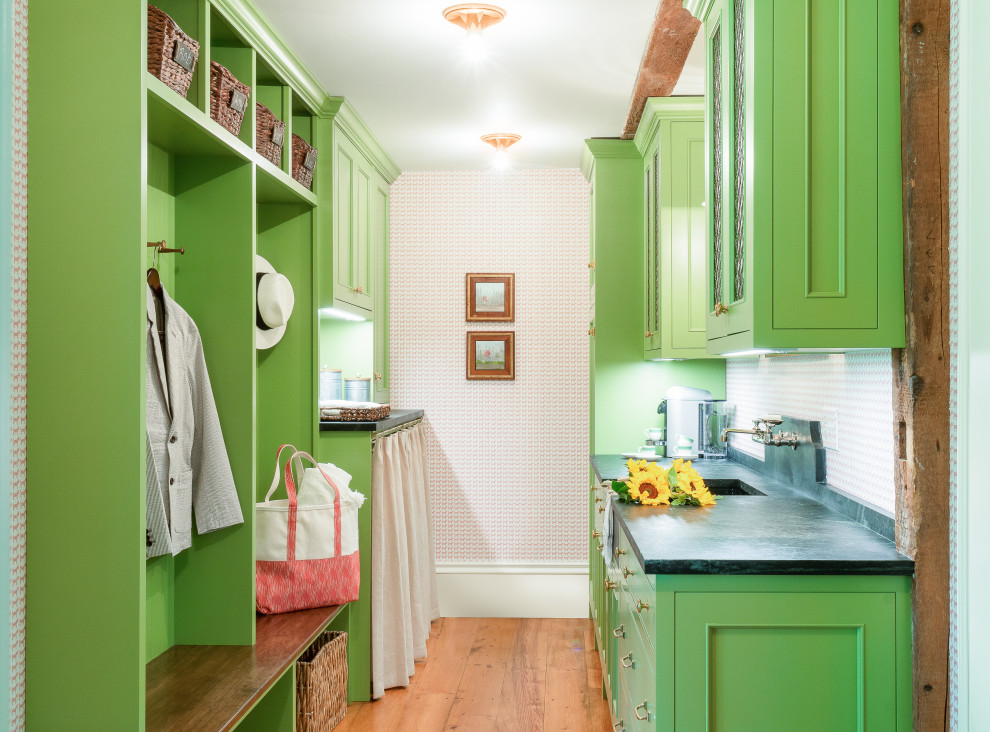 Example of a farmhouse galley medium tone wood floor, brown floor and wallpaper laundry room design in Boston with an integrated sink, recessed-panel cabinets, green cabinets, soapstone countertops, black countertops, pink walls and a side-by-side washer/dryer