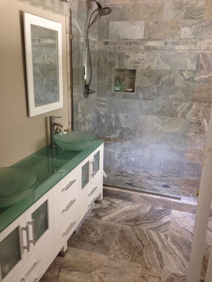 Photo of a mid-sized modern master bathroom in Other with glass-front cabinets, white cabinets, an alcove tub, an alcove shower, beige tile, stone tile, beige walls, porcelain floors, a vessel sink, glass benchtops, beige floor, a sliding shower screen and green benchtops.