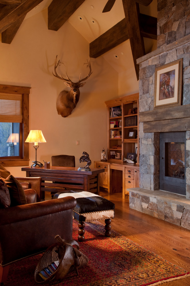 Inspiration for a large country study room in Other with beige walls, medium hardwood floors, a standard fireplace, a stone fireplace surround and a freestanding desk.
