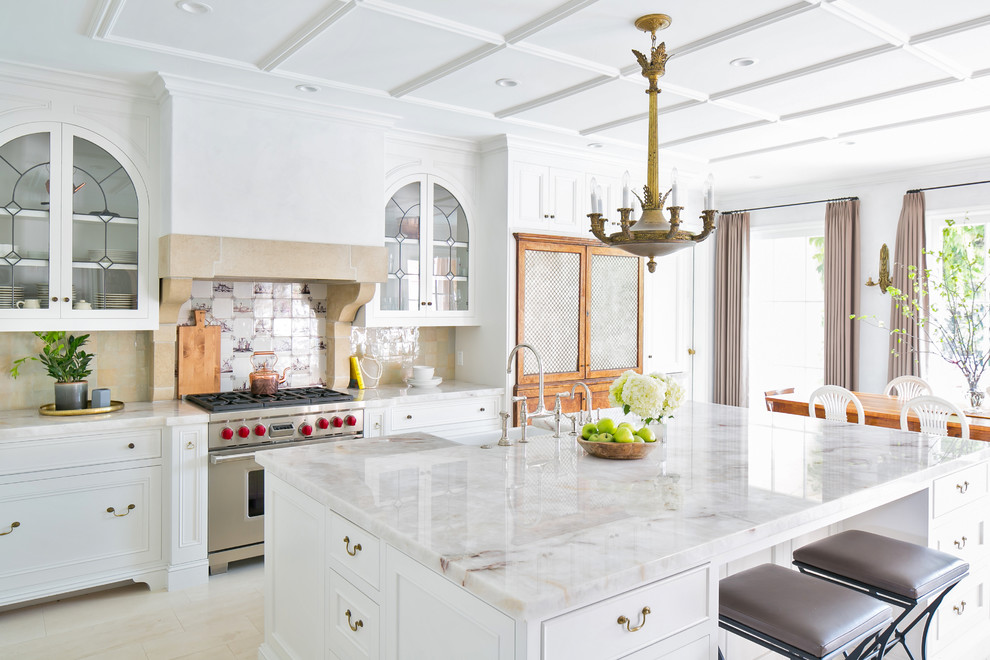 Inspiration for a large mediterranean l-shaped open plan kitchen in San Diego with a farmhouse sink, recessed-panel cabinets, white cabinets, marble benchtops, stainless steel appliances, with island, beige floor and multi-coloured benchtop.