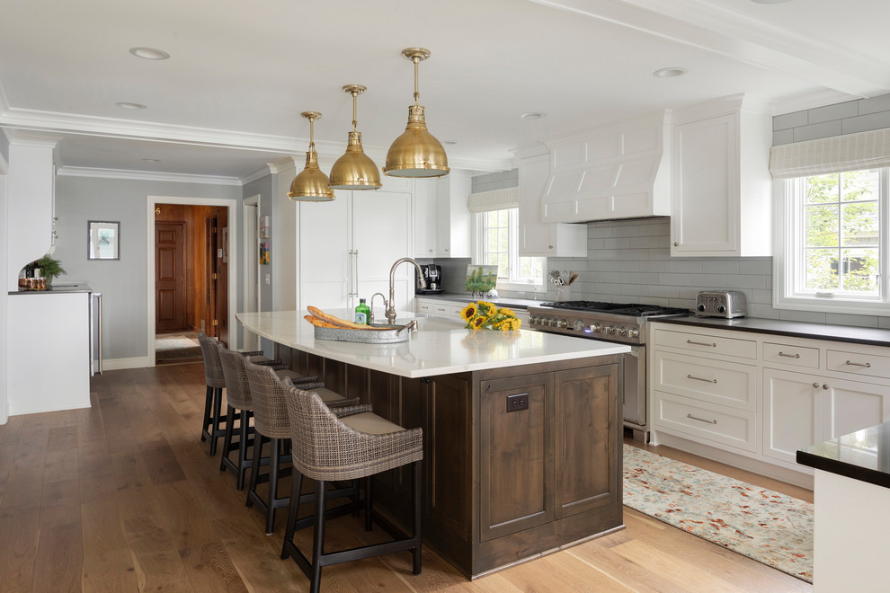Design ideas for a beach style kitchen in Minneapolis with shaker cabinets, white cabinets, grey splashback, subway tile splashback, stainless steel appliances, light hardwood floors, with island, beige floor and black benchtop.