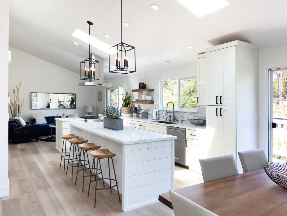 Eat-in kitchen - mid-sized transitional l-shaped vinyl floor, brown floor and vaulted ceiling eat-in kitchen idea with an undermount sink, shaker cabinets, white cabinets, quartz countertops, multicolored backsplash, mosaic tile backsplash, stainless steel appliances, an island and white countertops
