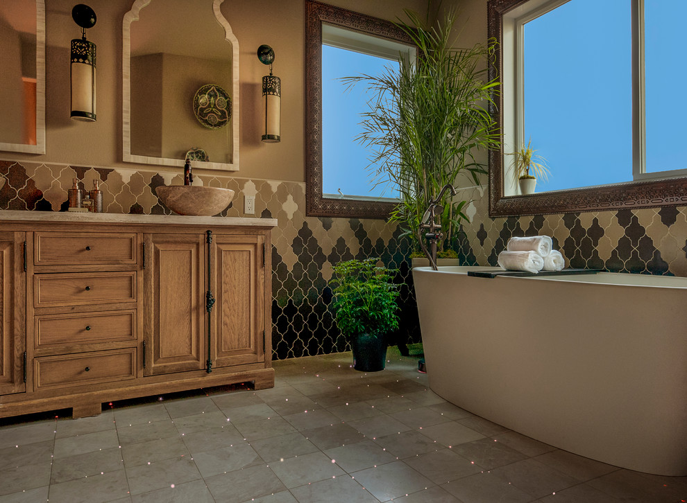 Bathroom in Seattle with furniture-like cabinets, light wood cabinets, a freestanding tub, multi-coloured tile, ceramic tile, beige walls, a vessel sink, marble benchtops and beige floor.