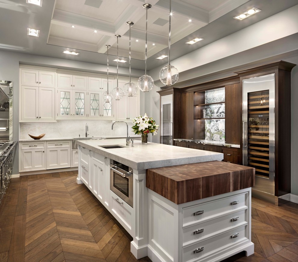 Example of a transitional medium tone wood floor kitchen design in Denver with an undermount sink, shaker cabinets, white cabinets, white backsplash, stainless steel appliances and two islands