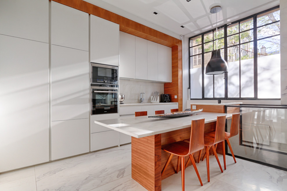 This is an example of a contemporary single-wall eat-in kitchen in Paris with flat-panel cabinets, white cabinets, white splashback, with island, an undermount sink and marble benchtops.