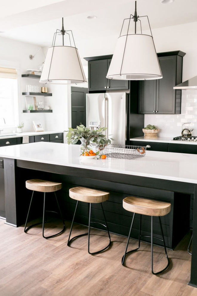 Inspiration for a mid-sized modern l-shaped kitchen in Columbus with a single-bowl sink, flat-panel cabinets, black cabinets, quartz benchtops, white splashback, subway tile splashback, stainless steel appliances, medium hardwood floors, with island, brown floor and white benchtop.
