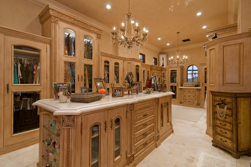 This is an example of an expansive traditional women's dressing room in Phoenix with glass-front cabinets, medium wood cabinets and travertine floors.