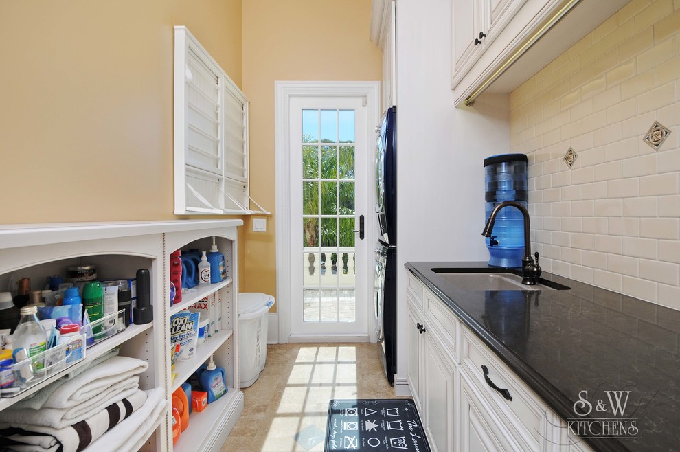 Large traditional galley dedicated laundry room in Tampa with an undermount sink, raised-panel cabinets, white cabinets, quartz benchtops, yellow walls, marble floors and a stacked washer and dryer.