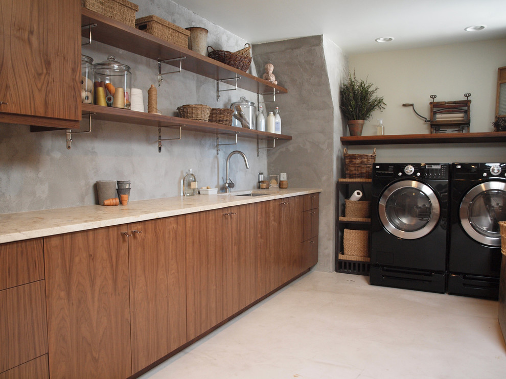 Photo of a mid-sized contemporary l-shaped utility room in Chicago with flat-panel cabinets, a side-by-side washer and dryer, an undermount sink, medium wood cabinets, limestone benchtops, grey walls, beige floor and beige benchtop.