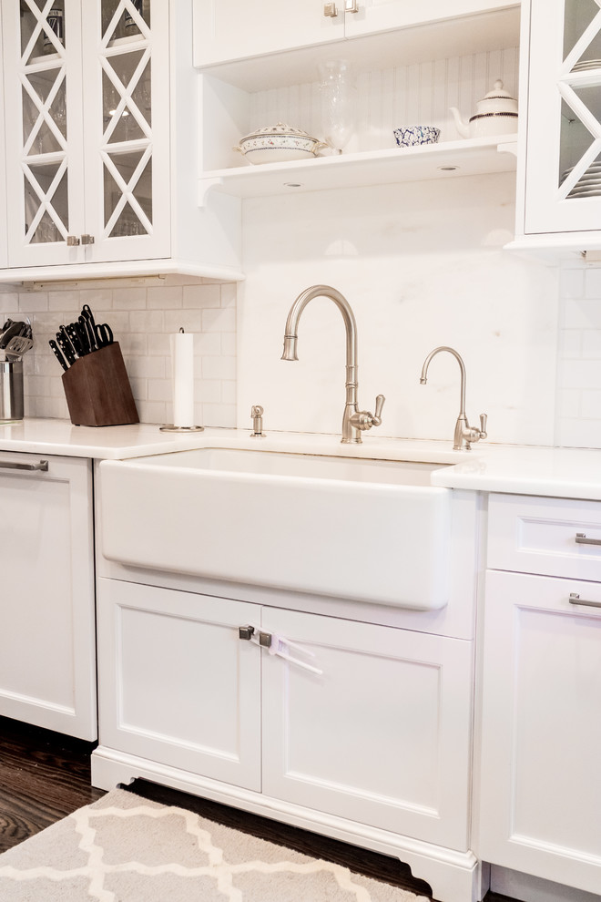 Mid-sized transitional dark wood floor and brown floor enclosed kitchen photo in New York with a farmhouse sink, recessed-panel cabinets, white cabinets, quartzite countertops, white backsplash, subway tile backsplash, stainless steel appliances and an island