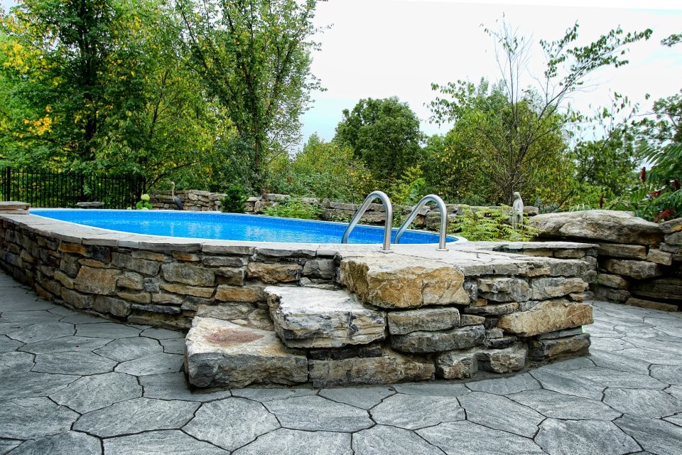 Design ideas for a mid-sized traditional backyard round aboveground pool in Ottawa with natural stone pavers.