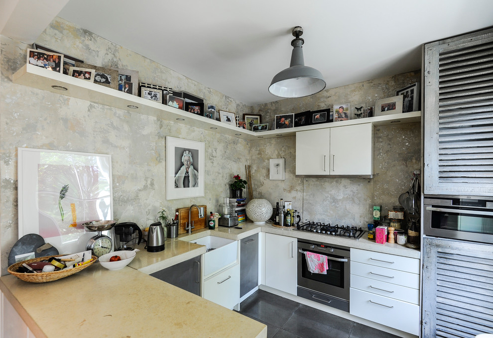 This is an example of a small eclectic u-shaped kitchen in London with a peninsula, flat-panel cabinets, white cabinets, concrete benchtops, multi-coloured splashback, stainless steel appliances and a farmhouse sink.