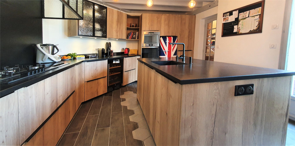 Idéer för att renovera ett stort funkis svart svart kök, med en integrerad diskho, släta luckor, skåp i ljust trä, granitbänkskiva, svart stänkskydd, integrerade vitvaror, cementgolv, en köksö och grått golv