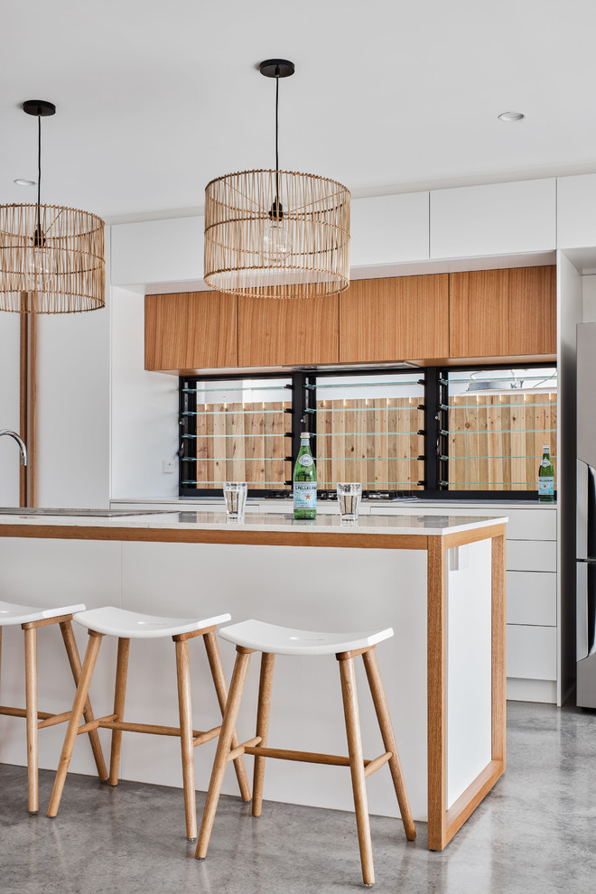 Inspiration for a beach style kitchen in Gold Coast - Tweed with a drop-in sink, flat-panel cabinets, medium wood cabinets, window splashback, stainless steel appliances, grey floor and white benchtop.