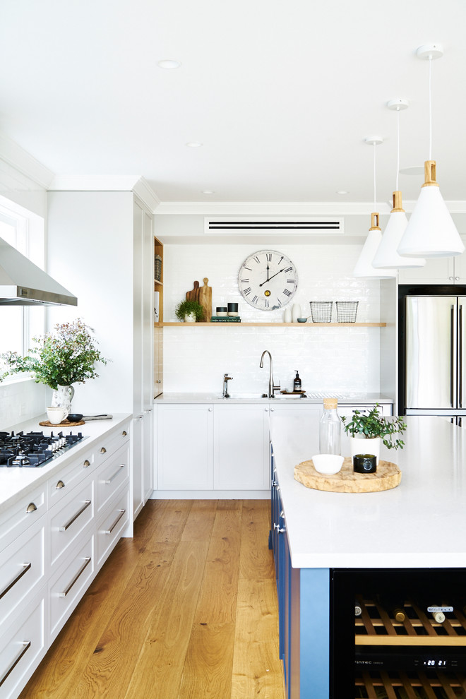 This is an example of a large transitional l-shaped open plan kitchen in Sydney with a drop-in sink, shaker cabinets, white cabinets, quartz benchtops, white splashback, subway tile splashback, stainless steel appliances, medium hardwood floors, with island and brown floor.