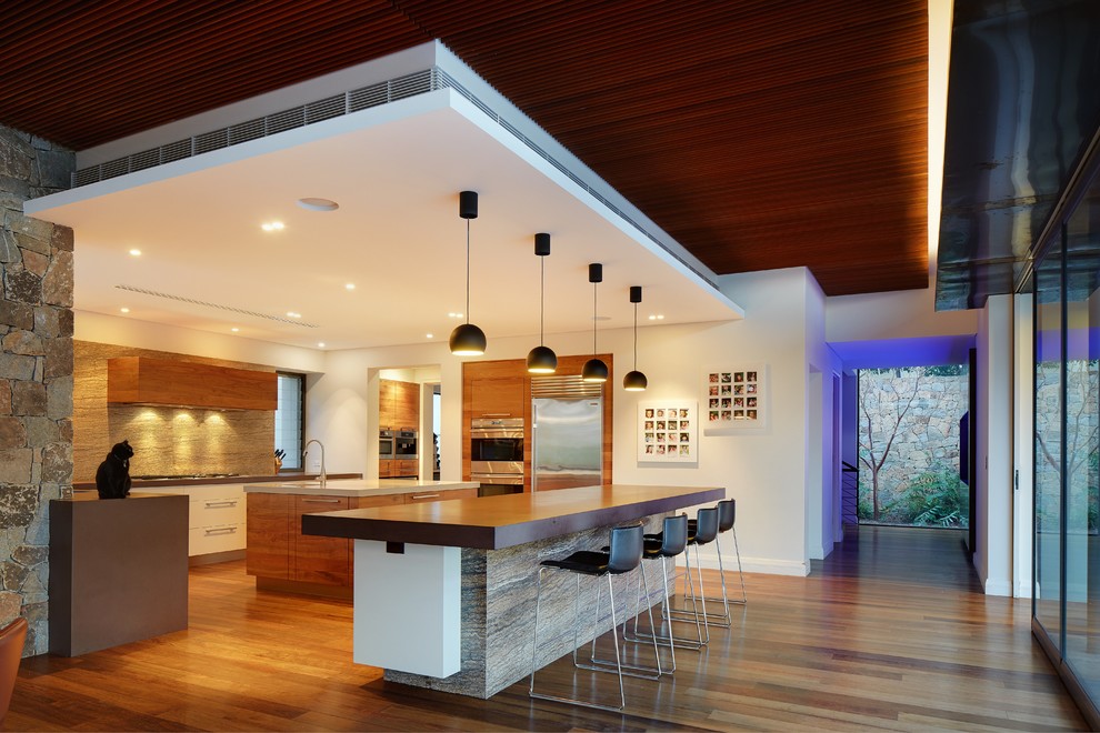 Photo of a large contemporary single-wall eat-in kitchen in Perth with a drop-in sink, flat-panel cabinets, brown cabinets, marble benchtops, beige splashback, limestone splashback, stainless steel appliances, light hardwood floors, multiple islands and brown floor.