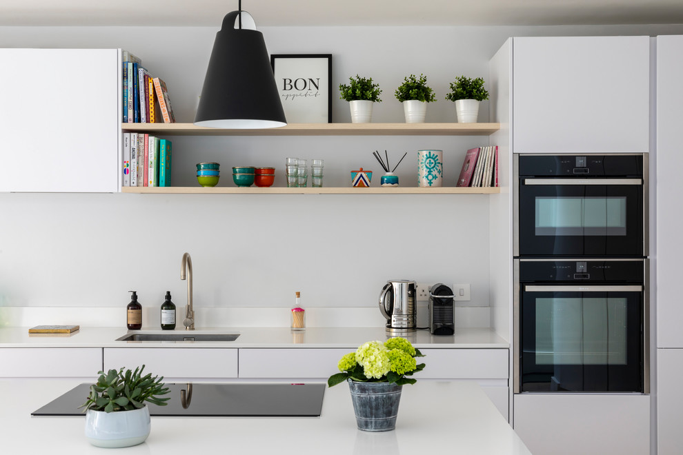 Design ideas for a contemporary eat-in kitchen in London with flat-panel cabinets, white cabinets, limestone benchtops, white splashback, limestone splashback, black appliances, with island, white benchtop and an undermount sink.
