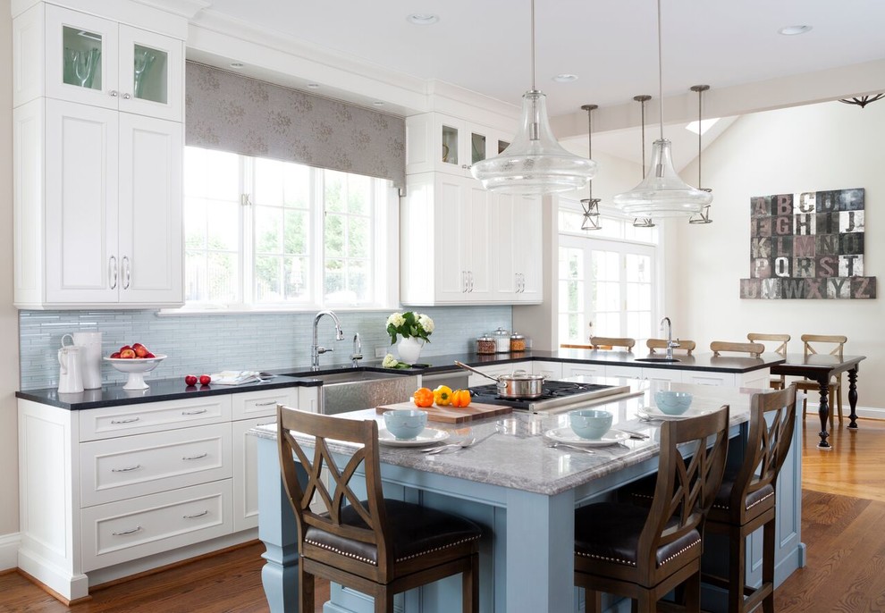 Open concept kitchen - mid-sized transitional l-shaped medium tone wood floor open concept kitchen idea in DC Metro with a farmhouse sink, beaded inset cabinets, white cabinets, limestone countertops, blue backsplash, matchstick tile backsplash, stainless steel appliances and an island