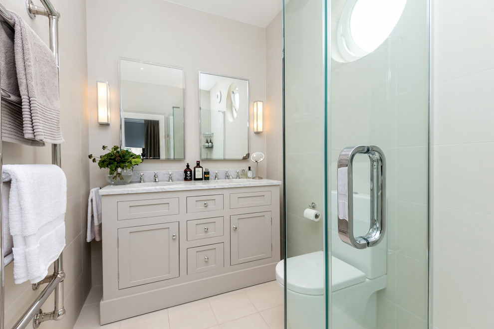 Design ideas for a small transitional master bathroom in London with shaker cabinets, grey cabinets, a corner shower, a two-piece toilet, beige tile, stone tile, beige walls, porcelain floors, a drop-in sink, marble benchtops, beige floor, a hinged shower door, grey benchtops, a double vanity and a built-in vanity.