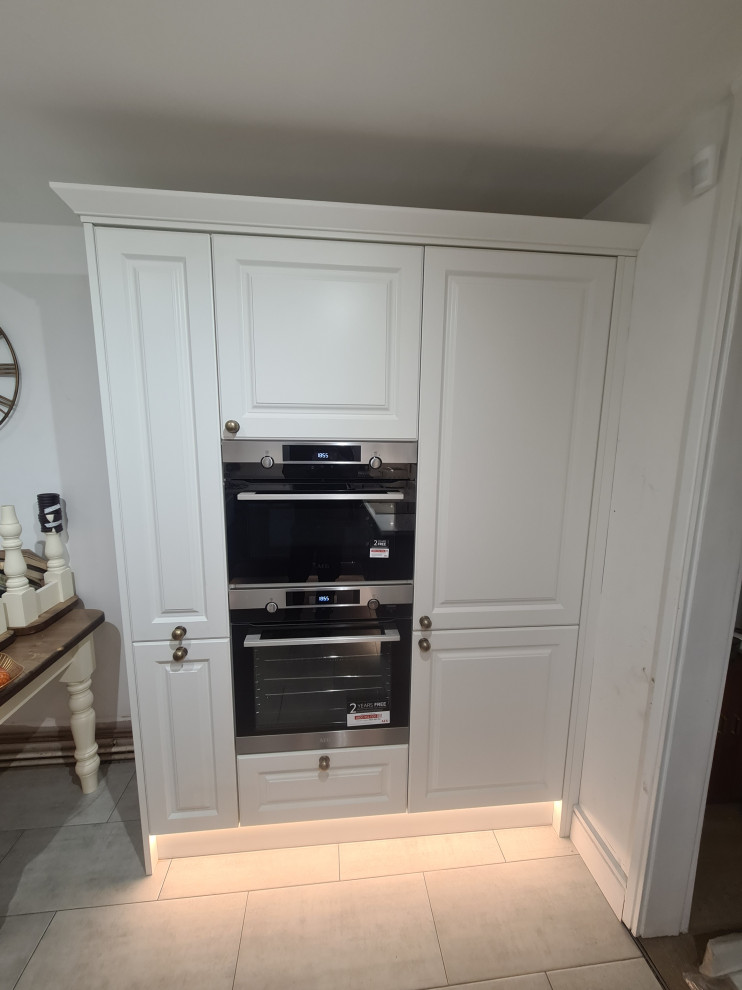 Inspiration for a large victorian grey and white u-shaped open plan kitchen in London with a belfast sink, shaker cabinets, white cabinets, quartz worktops, white splashback, ceramic splashback, integrated appliances, ceramic flooring, grey floors, white worktops and feature lighting.
