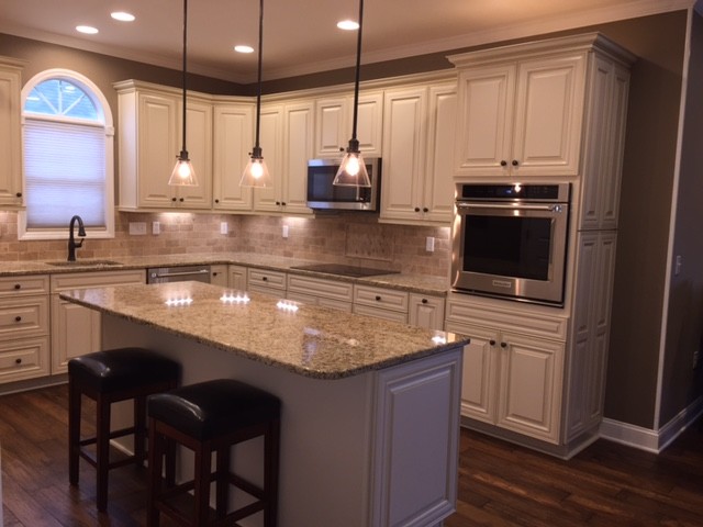 Example of a mid-sized transitional l-shaped dark wood floor kitchen design with an undermount sink, raised-panel cabinets, white cabinets, granite countertops, beige backsplash, stone tile backsplash, stainless steel appliances and an island