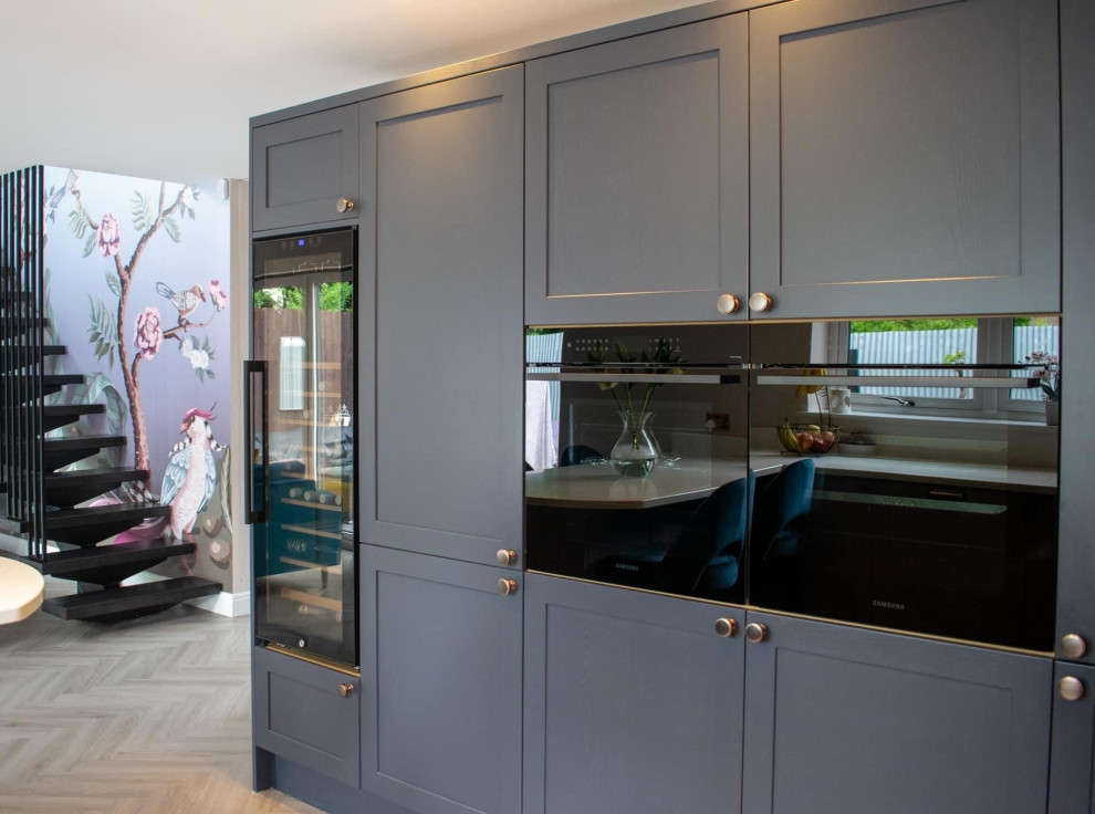 Immagine di una cucina moderna di medie dimensioni con lavello integrato, ante in stile shaker, ante blu, top in quarzite, paraspruzzi bianco, elettrodomestici neri, penisola, pavimento marrone e top bianco