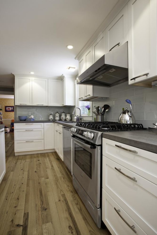 Eat-in kitchen - mid-sized transitional l-shaped medium tone wood floor eat-in kitchen idea with flat-panel cabinets, white cabinets, solid surface countertops, stainless steel appliances, white walls and an island