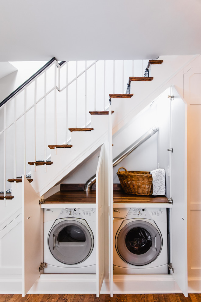 Inspiration for a mid-sized traditional single-wall laundry cupboard in DC Metro with shaker cabinets, white cabinets, wood benchtops, white walls, dark hardwood floors, a concealed washer and dryer, brown floor and brown benchtop.