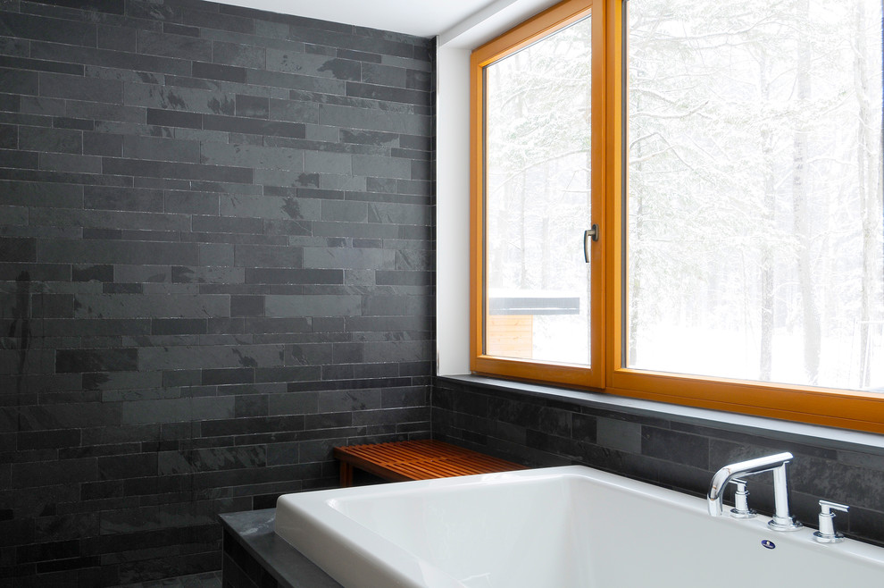 This is an example of a contemporary master bathroom in Toronto with flat-panel cabinets, a drop-in tub, black tile, slate, black walls, slate floors and black floor.