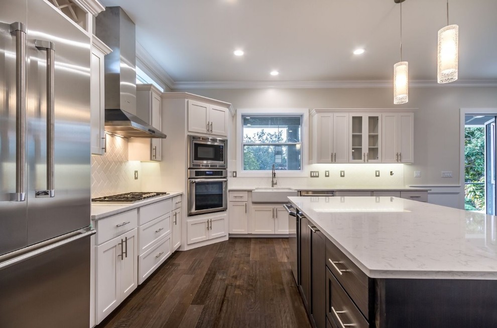 Large transitional l-shaped open plan kitchen in Tampa with a farmhouse sink, shaker cabinets, dark wood cabinets, quartzite benchtops, white splashback, porcelain splashback, stainless steel appliances, dark hardwood floors and with island.