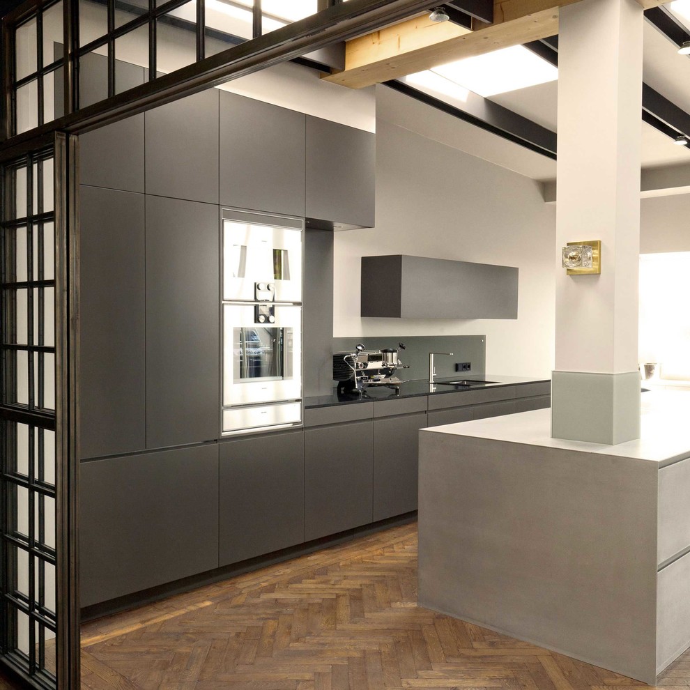 Design ideas for a large eclectic open plan kitchen in Berlin with stainless steel appliances, medium hardwood floors, flat-panel cabinets, grey cabinets, grey splashback, with island and a single-bowl sink.