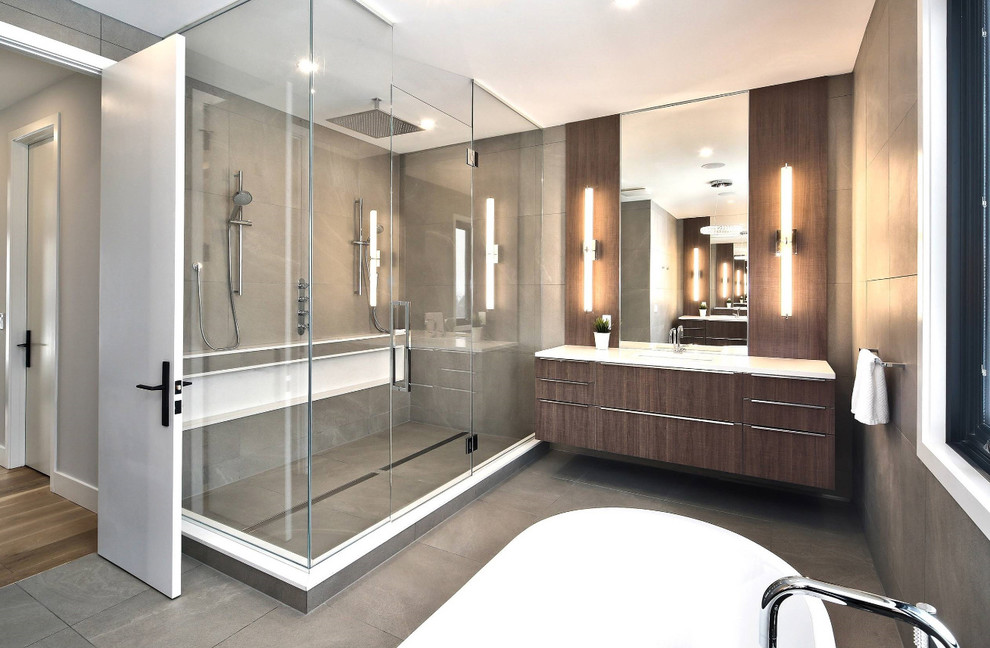 Expansive contemporary master bathroom in Toronto with flat-panel cabinets, brown cabinets, a freestanding tub, a double shower, a one-piece toilet, gray tile, porcelain tile, grey walls, porcelain floors, an undermount sink, quartzite benchtops, grey floor, a hinged shower door and white benchtops.
