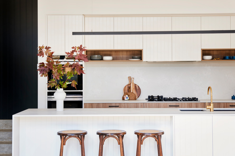 Design ideas for a large contemporary l-shaped kitchen in Geelong with an undermount sink, flat-panel cabinets, white cabinets, white splashback, black appliances, concrete floors, with island, grey floor and white benchtop.