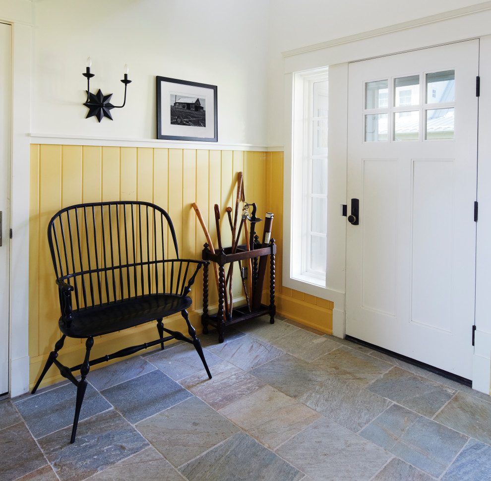Lantlig inredning av ett kapprum, med gula väggar, skiffergolv, en enkeldörr, en vit dörr och flerfärgat golv