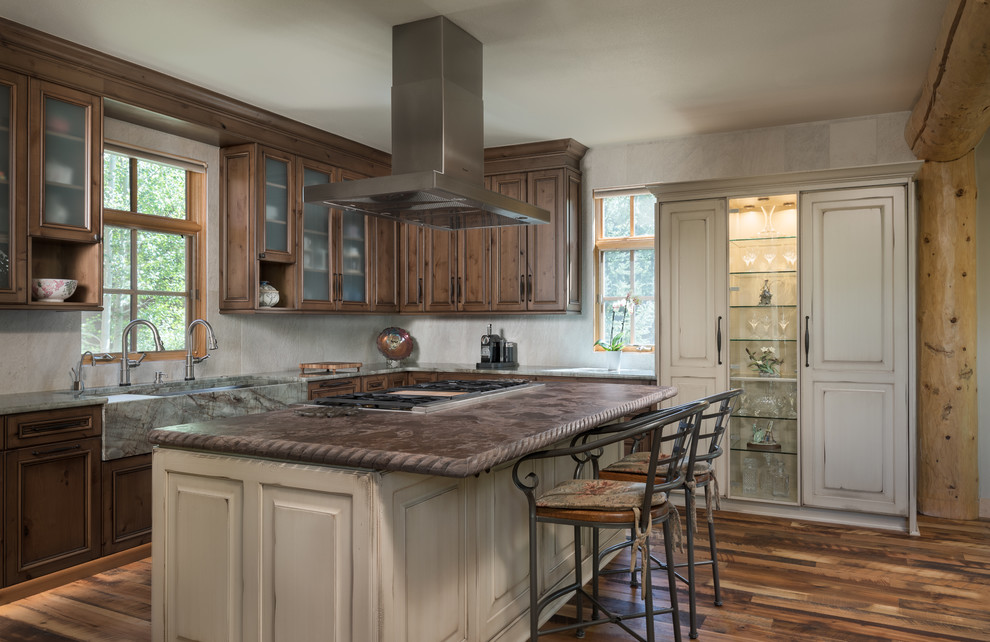 Inspiration for a large country l-shaped open plan kitchen in Other with glass-front cabinets, distressed cabinets, quartzite benchtops, beige splashback, ceramic splashback, stainless steel appliances, dark hardwood floors, with island, brown floor and a farmhouse sink.
