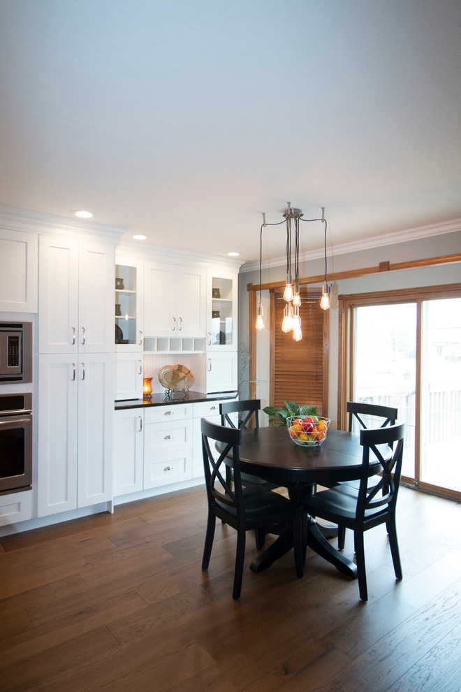 Large transitional l-shaped medium tone wood floor eat-in kitchen photo with an undermount sink, shaker cabinets, white cabinets, granite countertops, gray backsplash, stone tile backsplash, stainless steel appliances and an island