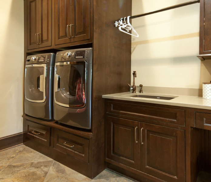 This is an example of a large single-wall laundry cupboard in Miami with dark wood cabinets, solid surface benchtops, beige walls, porcelain floors, a side-by-side washer and dryer, raised-panel cabinets and an undermount sink.