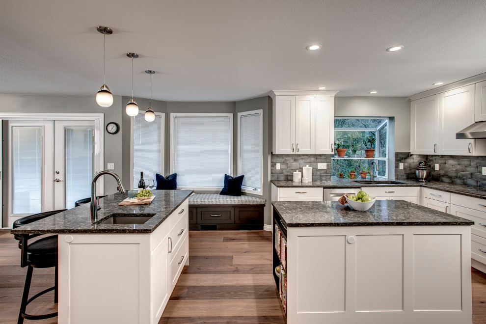 Mid-sized transitional l-shaped medium tone wood floor and brown floor eat-in kitchen photo in Seattle with a double-bowl sink, shaker cabinets, white cabinets, quartz countertops, gray backsplash, ceramic backsplash, stainless steel appliances, two islands and gray countertops