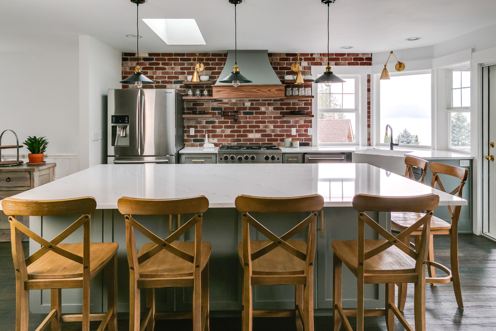 Photo of a small country l-shaped open plan kitchen in Seattle with a farmhouse sink, shaker cabinets, grey cabinets, quartzite benchtops, red splashback, brick splashback, stainless steel appliances, dark hardwood floors, with island, brown floor and white benchtop.