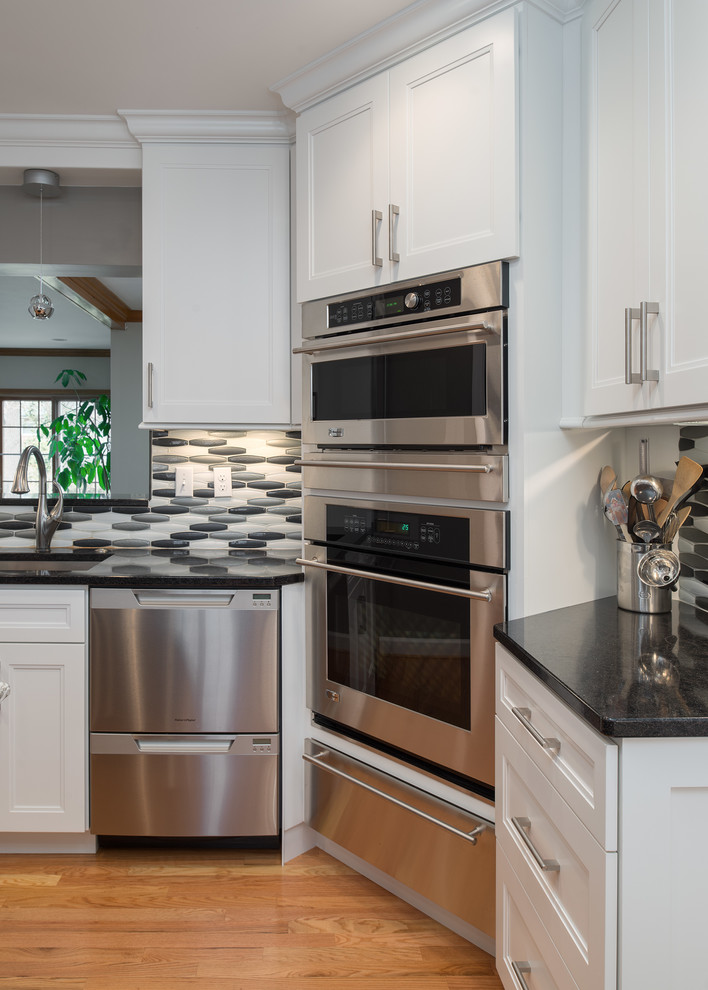 Example of a transitional l-shaped light wood floor eat-in kitchen design in St Louis with an undermount sink, shaker cabinets, white cabinets, quartz countertops, metallic backsplash, glass tile backsplash, stainless steel appliances and an island