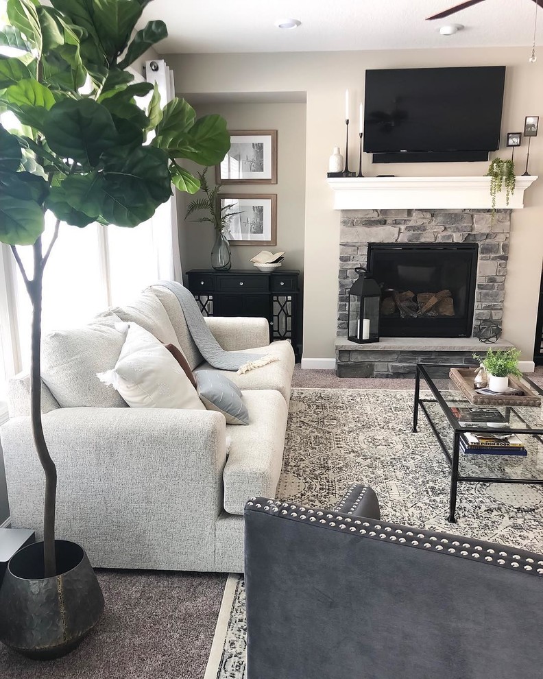 This is an example of a large transitional open concept living room in Minneapolis with beige walls, carpet, a standard fireplace, a stone fireplace surround, a wall-mounted tv and grey floor.