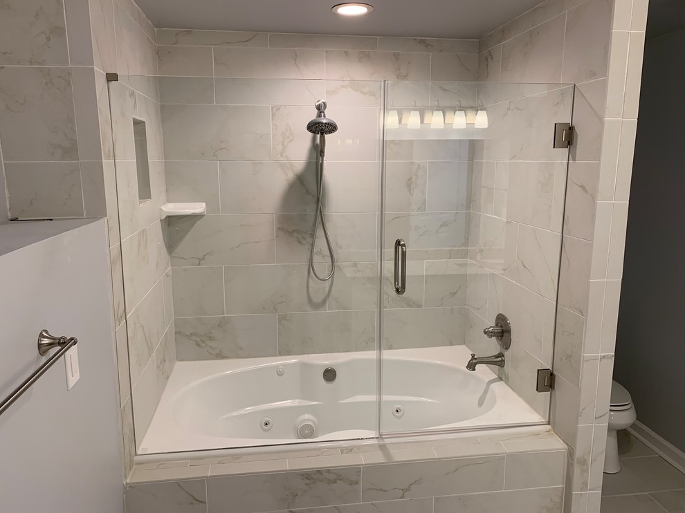 Inspiration for a mid-sized transitional master bathroom in Atlanta with a hot tub, a shower/bathtub combo, gray tile, marble, grey walls, porcelain floors, grey floor and a hinged shower door.