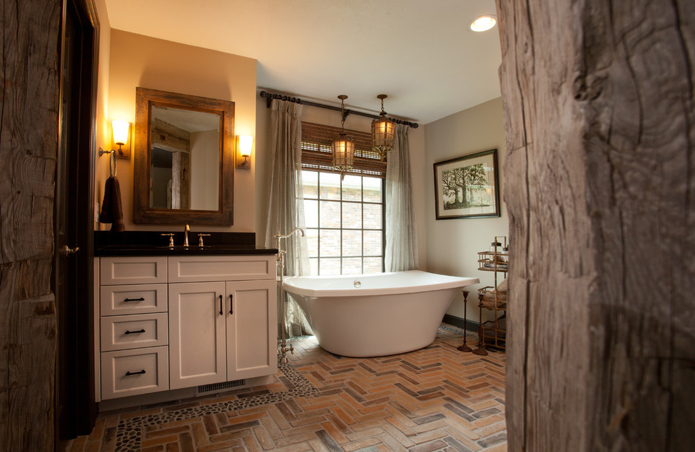 Inspiration for a mid-sized country master bathroom in Other with shaker cabinets, white cabinets, a freestanding tub, beige walls, brick floors and an undermount sink.