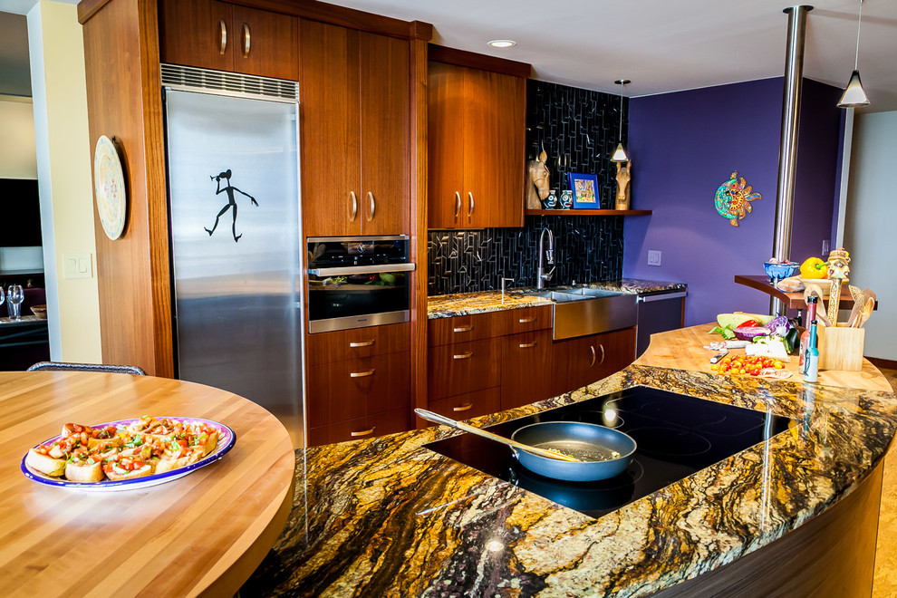 Inspiration for a large eclectic galley kitchen in Portland with a farmhouse sink, flat-panel cabinets, medium wood cabinets, granite benchtops, black splashback, marble splashback, stainless steel appliances, cork floors and purple benchtop.