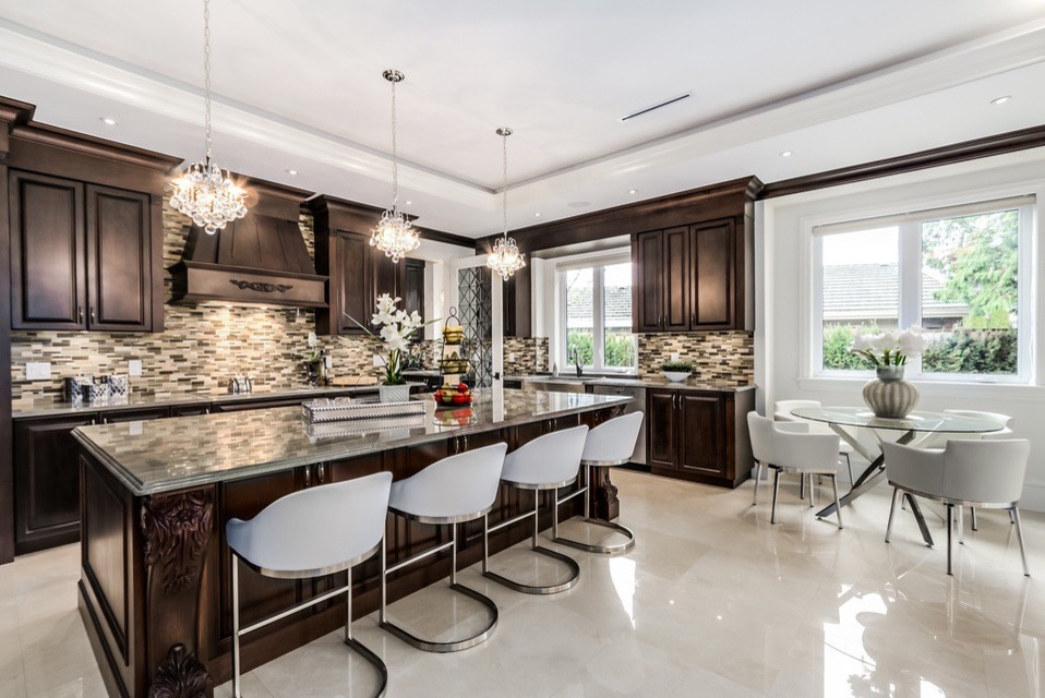 This is an example of a large transitional l-shaped eat-in kitchen in Vancouver with a farmhouse sink, recessed-panel cabinets, dark wood cabinets, marble benchtops, multi-coloured splashback, matchstick tile splashback, stainless steel appliances, marble floors, with island and beige floor.