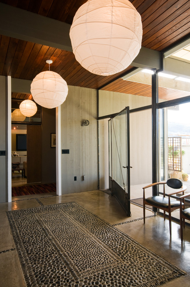 Photo of a midcentury foyer in Other with concrete floors, a pivot front door and a glass front door.