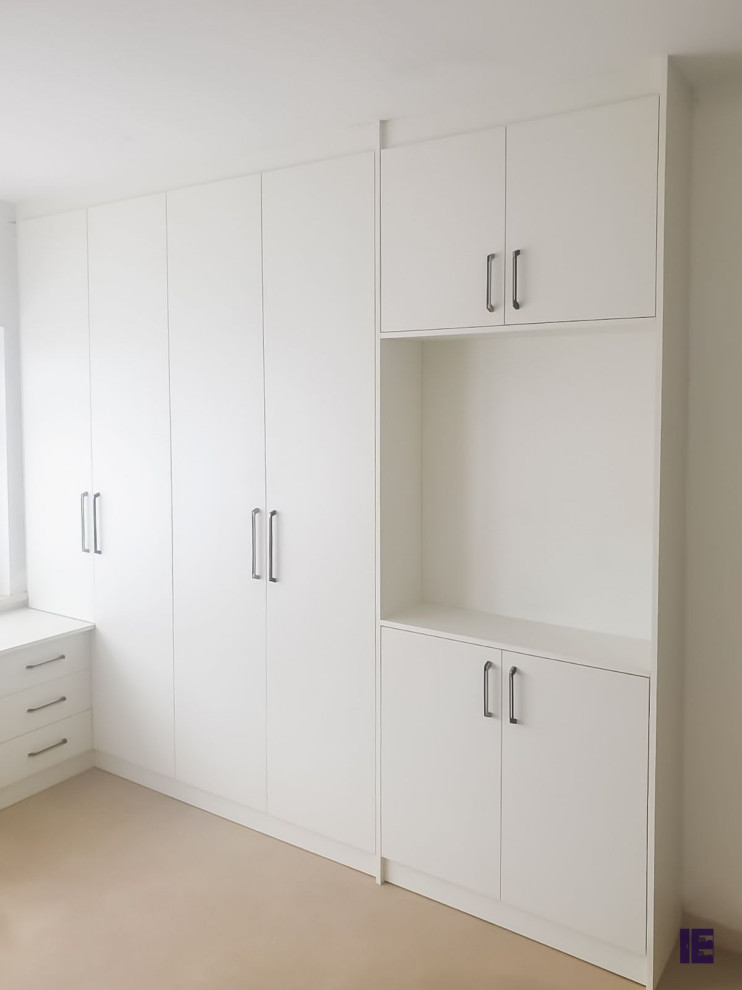 This is an example of a large modern built-in wardrobe in London with flat-panel cabinets and white cabinets.